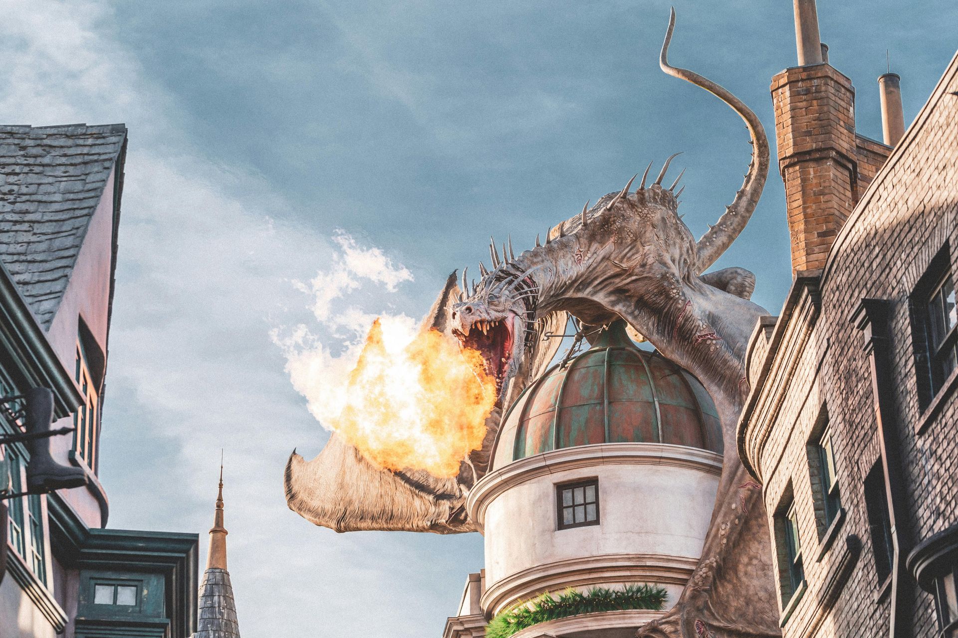 Dragon breathes fire over a building in a town, smoke and flames visible.