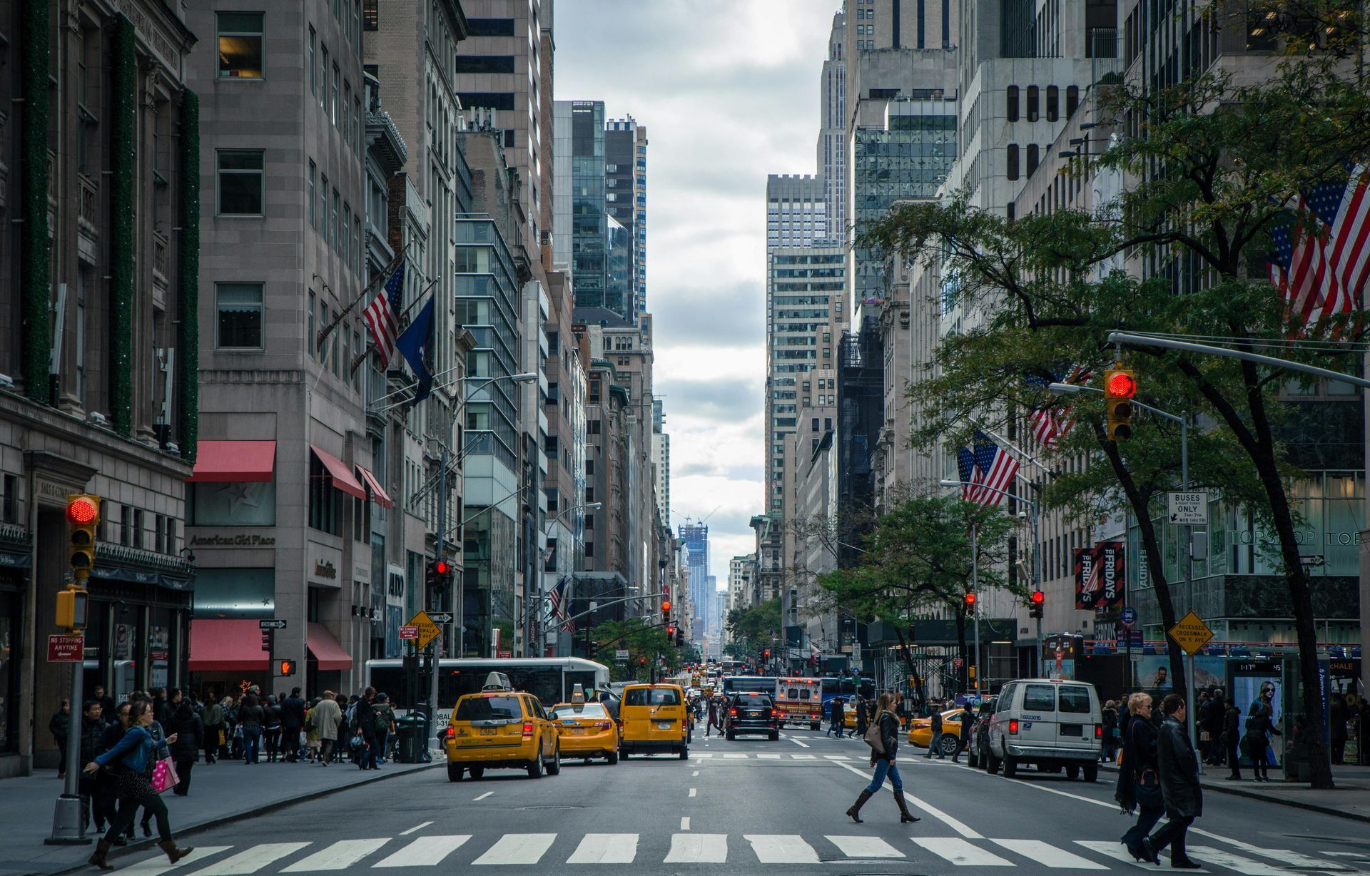 Busy New York City street with yellow taxis, pedestrians, and tall buildings under a cloudy sky.