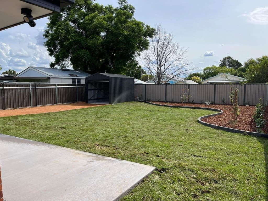Backyard with green grass, shed, wooden fence, and concrete patio — Darlington Landscaping in Dubbo, NSW