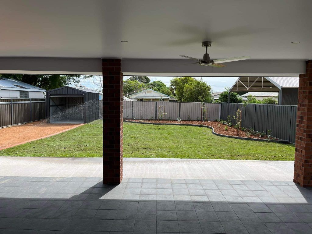 View from a covered patio of a backyard with a fence, green grass, and a shed — Darlington Landscaping in Dubbo, NSW