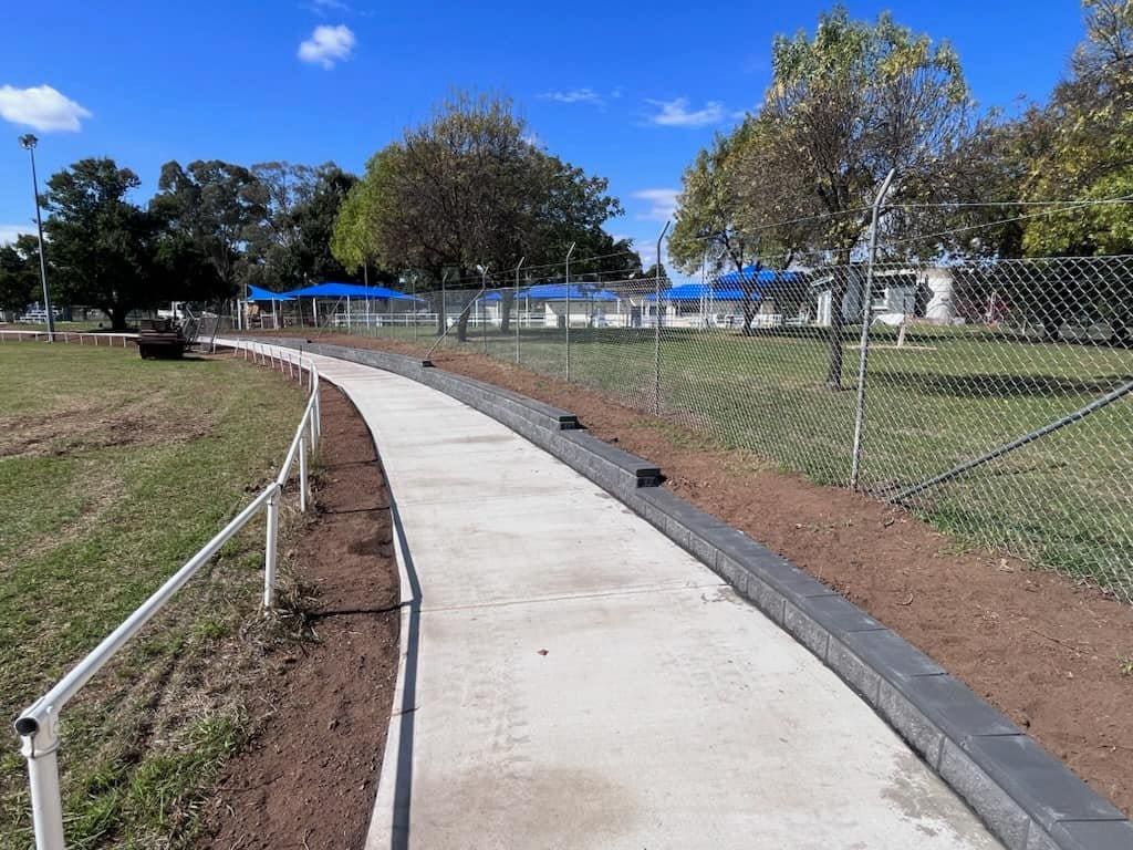 A paved walkway with metal railings and a chain link fence, bordered by grass and trees, under a blue sky — Darlington Landscaping in Dubbo, NSW