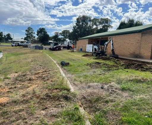 Construction site near a brick building, with trucks, an excavator, and a grassy area — Darlington Landscaping in Dubbo, NSW