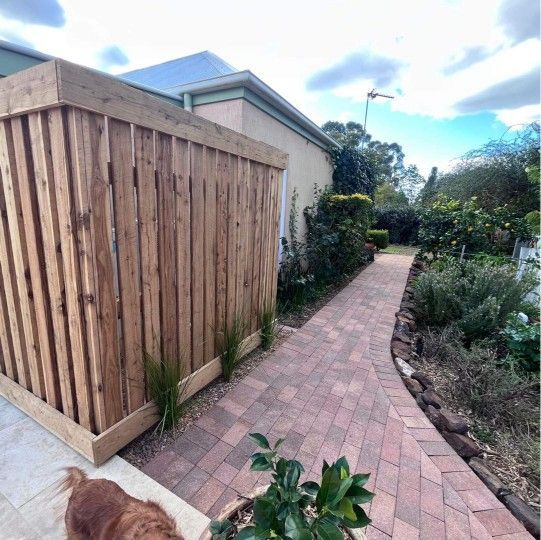 Wooden fence next to a brick path leading to a garden, with a dog in view — Darlington Landscaping in Dubbo, NSW