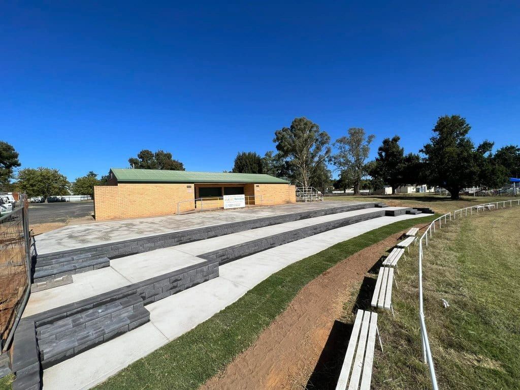 Outdoor amphitheater with brick building, grass, and tiered seating under a bright blue sky — Darlington Landscaping in Dubbo, NSW