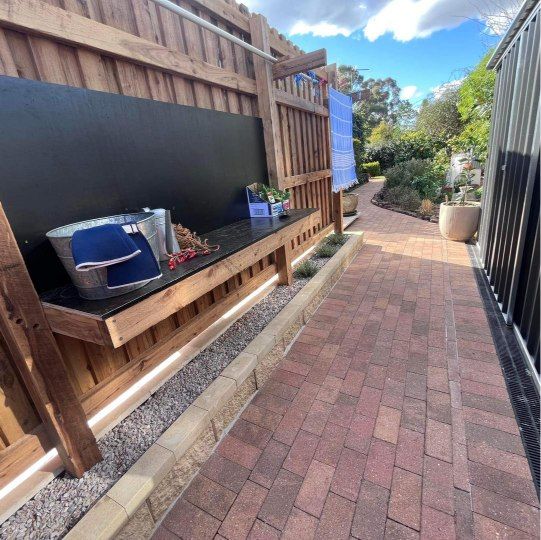 Brick pathway next to a wooden bench and fence with a blue sky overhead — Darlington Landscaping in Dubbo, NSW