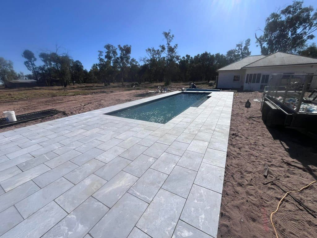 Rectangular pool with grey pavers, set in a dry dirt yard with a house in the background, under a blue sky — Darlington Landscaping in Dubbo, NSW