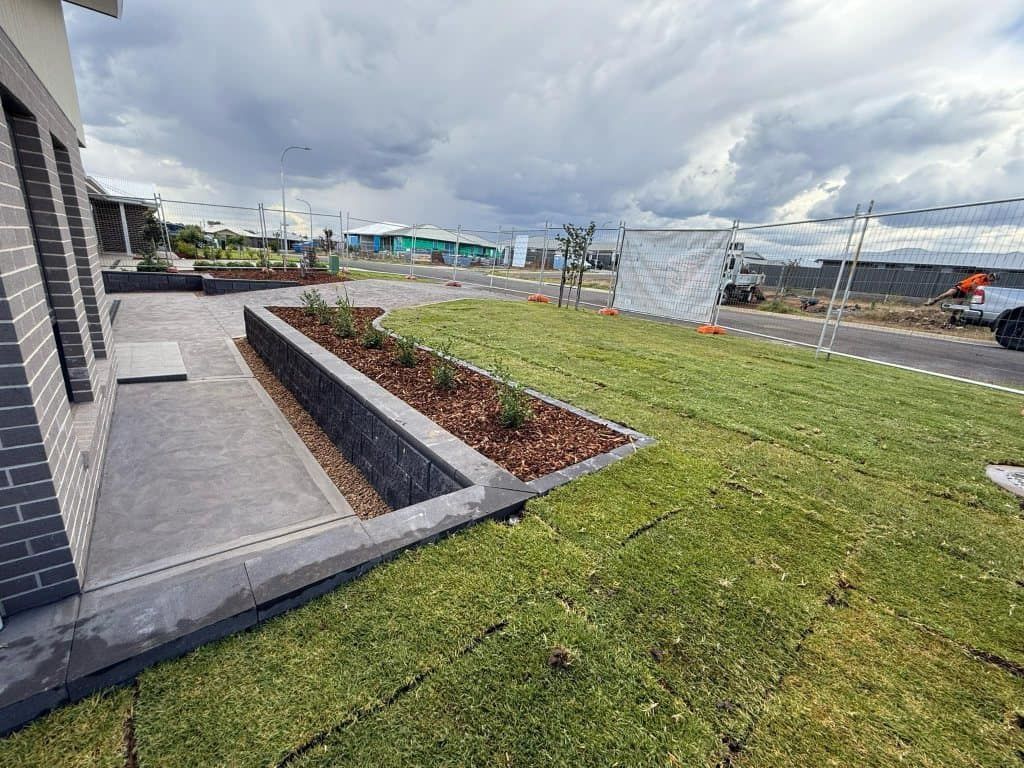 Newly landscaped front yard with grey retaining wall, green grass, and cloudy sky — Darlington Landscaping in Dubbo, NSW
