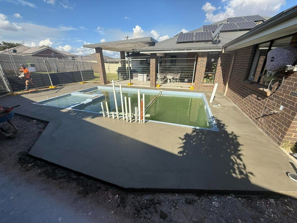 Pool construction with concrete work in progress near a brick house under a cloudy sky — Darlington Landscaping in Dubbo, NSW