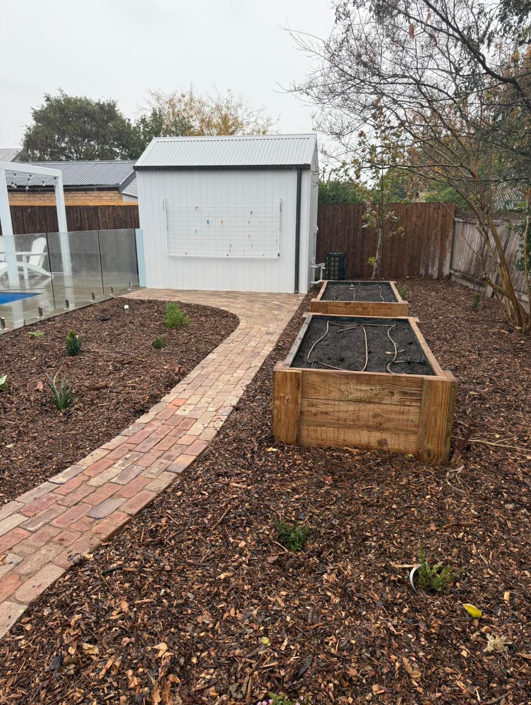 Brick path leads to a white shed, past raised wooden garden beds in a backyard — Darlington Landscaping in Dubbo, NSW