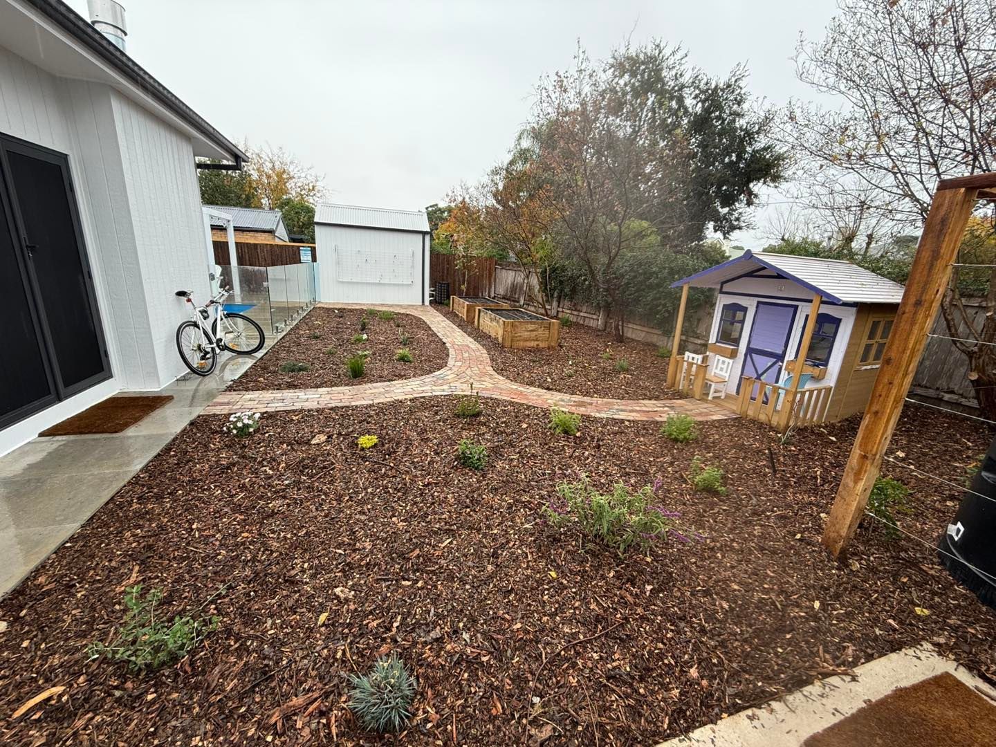 Backyard with a playhouse, brick pathways, garden beds, and a bicycle — Darlington Landscaping in Dubbo, NSW
