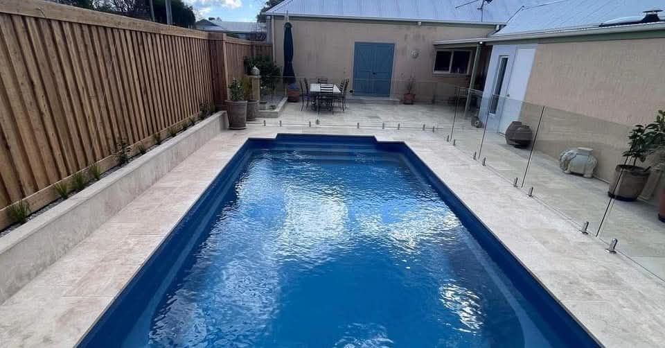 A blue rectangular swimming pool in a backyard with glass fencing, concrete patio, and wooden fence — Darlington Landscaping in Dubbo, NSW
