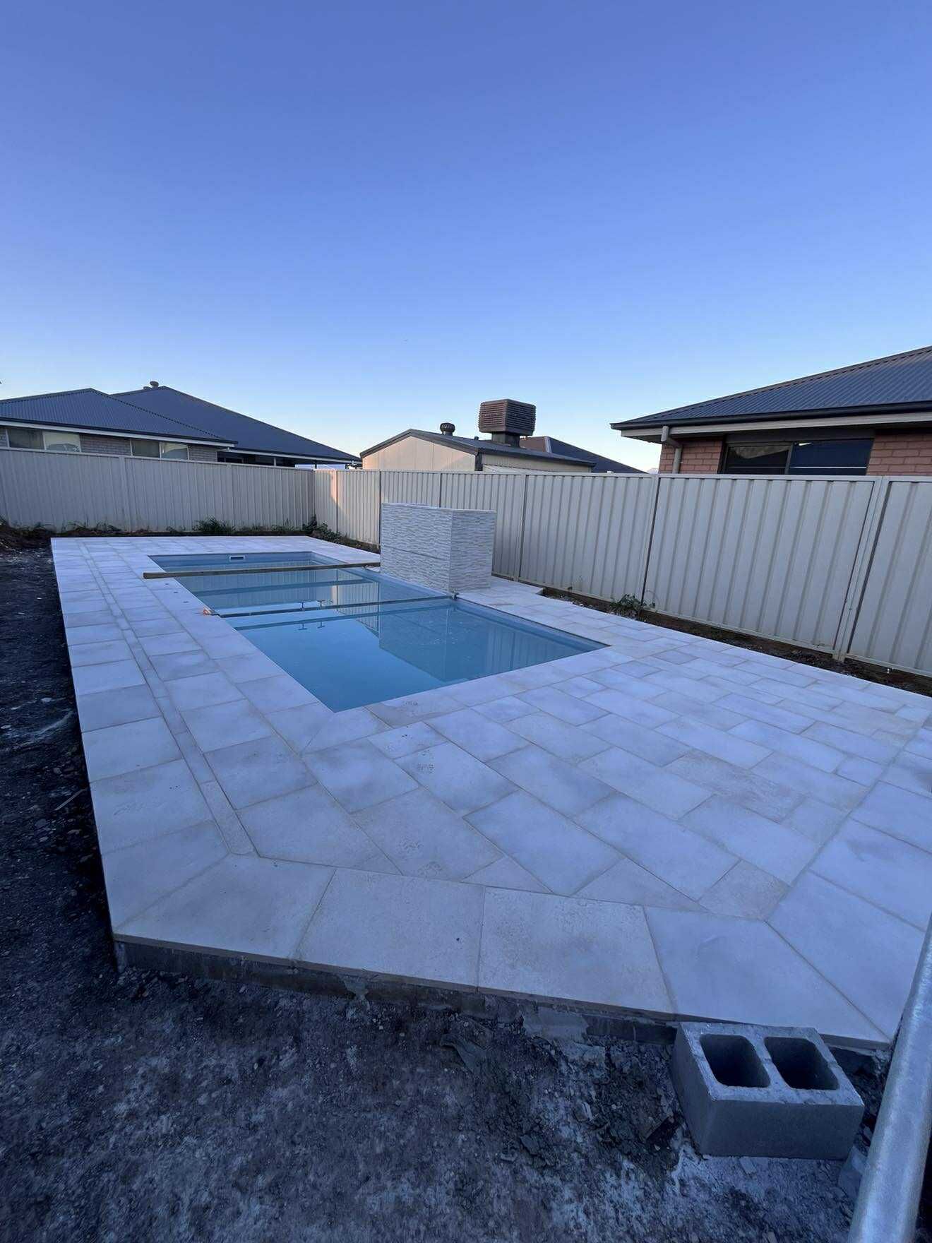 A rectangular pool with light tiles and a stone wall, surrounded by a backyard with a fence — Darlington Landscaping in Dubbo, NSW