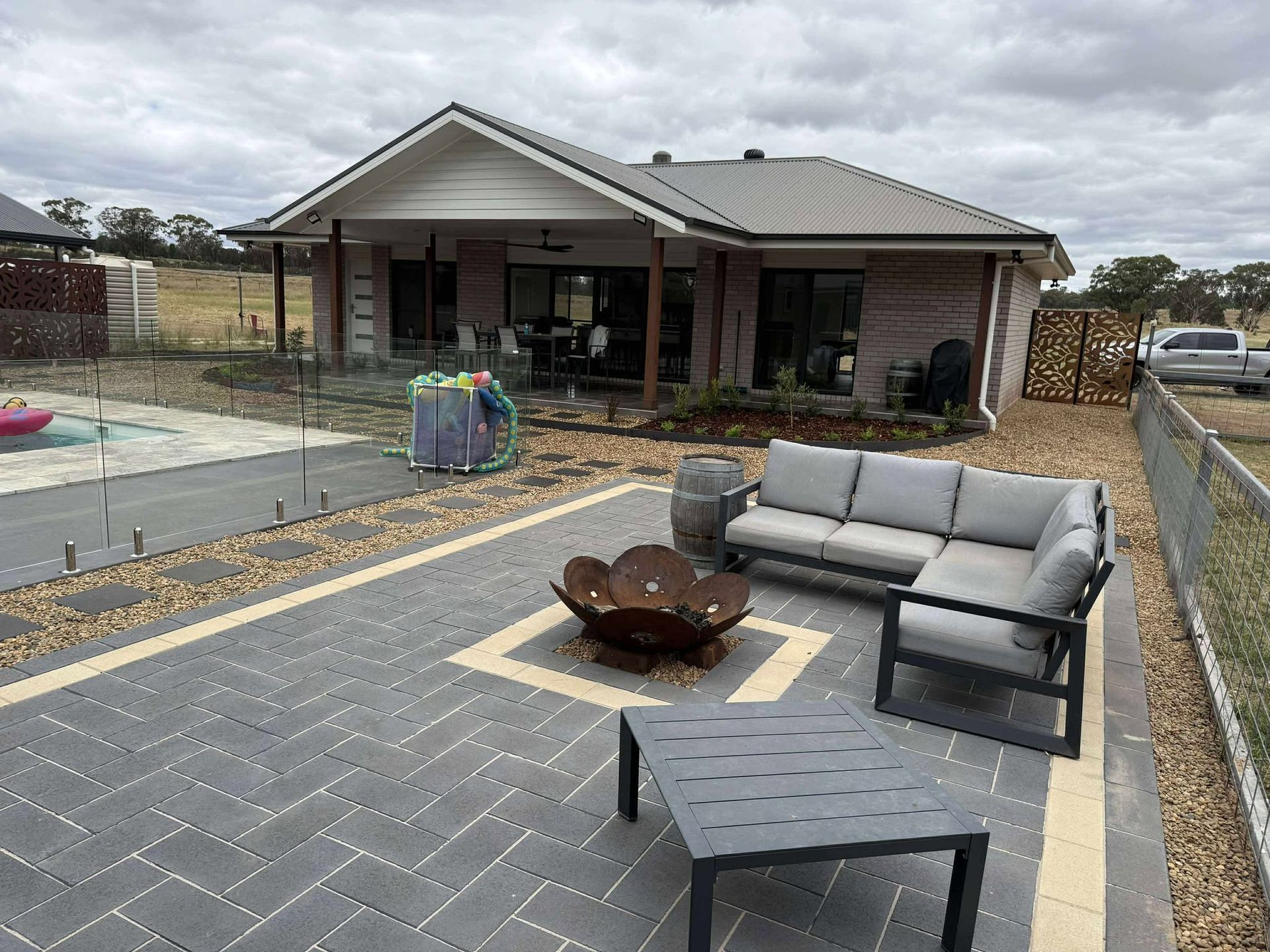 Outdoor patio with gray furniture, fire pit, and house in background — Darlington Landscaping in Dubbo, NSW