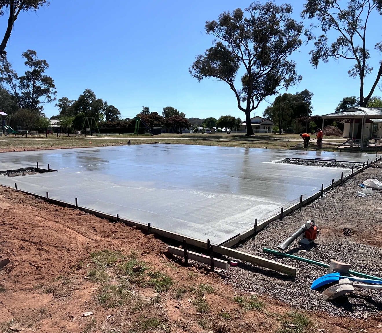Freshly poured concrete slab, construction site. Two workers in orange shirts, bright sunny day — Darlington Landscaping in Dubbo, NSW