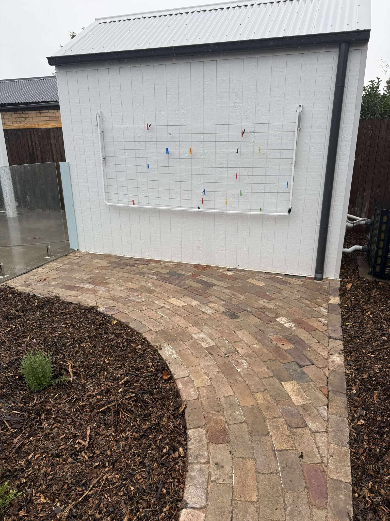 Brick pathway curves toward a white building with a metal roof and a metal trellis on its facade — Darlington Landscaping in Dubbo, NSW