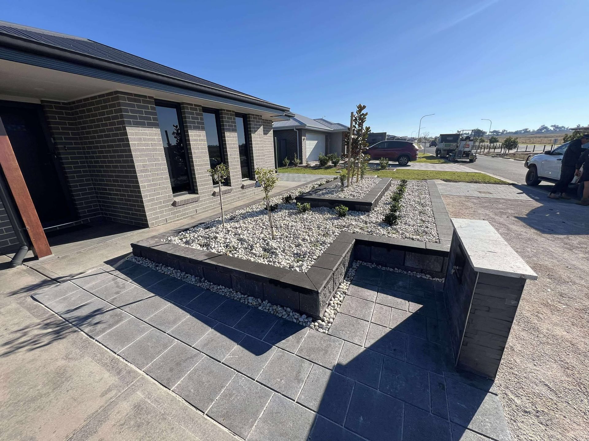 House with grey brick exterior, stone garden bed, and paving in a sunny setting — Darlington Landscaping in Wellington, NSW