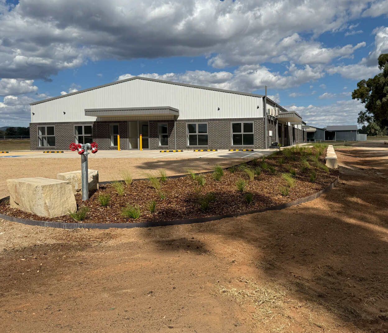 A light-colored metal building with windows on a slight hill under a blue sky with some clouds — Darlington Landscaping in Warren, NSW