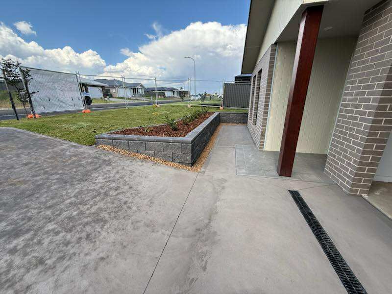 Concrete driveway leads to a house with a brick column and a raised garden bed under a cloudy sky — Darlington Landscaping in Dubbo, NSW