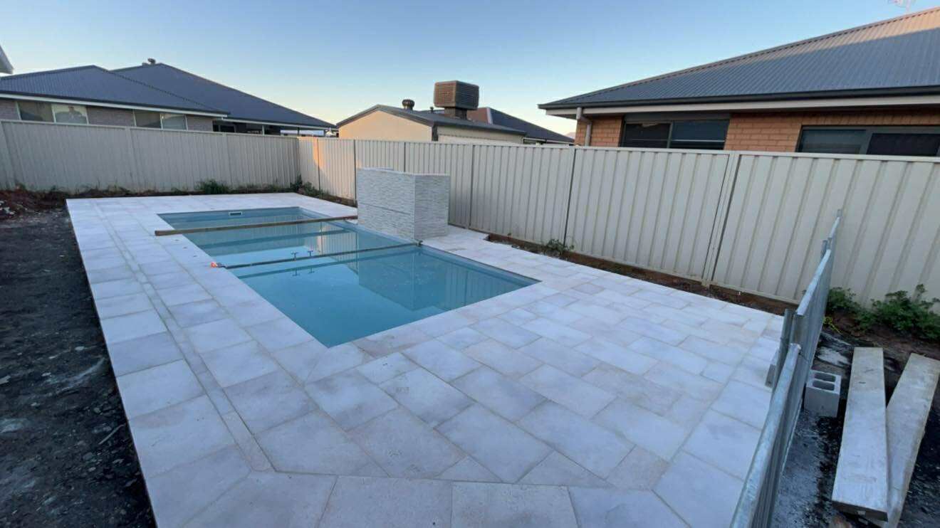 A rectangular swimming pool surrounded by light-colored paving, next to a white fence, in a backyard — Darlington Landscaping in Nyngan, NSW