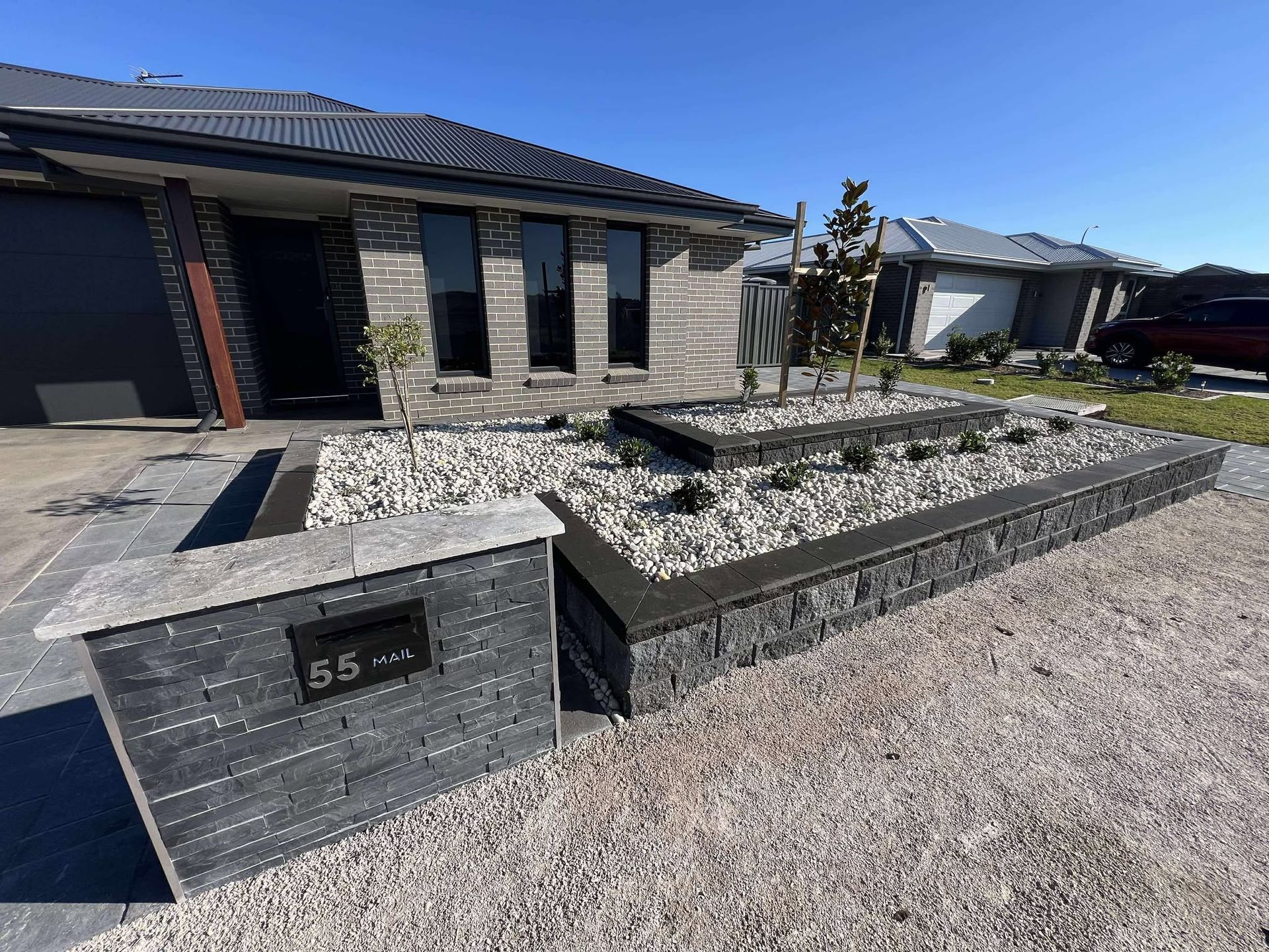 Modern home with landscaped front yard; black brick, raised garden beds with white stones, grry driveway  — Darlington Landscaping in Narromine, NSW