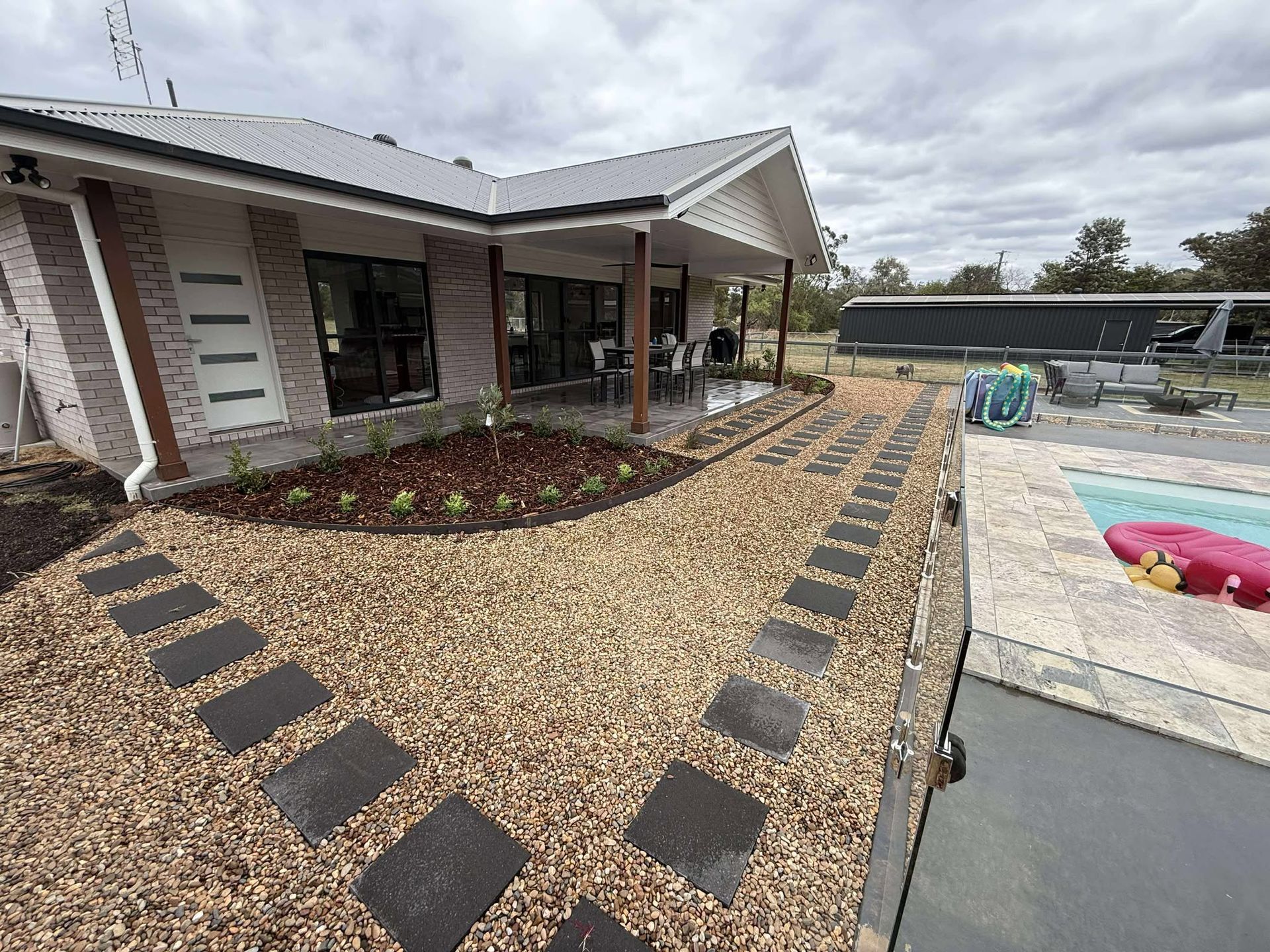 A house with a gravel path, stepping stones, and a swimming pool on a cloudy day — Darlington Landscaping in Dubbo, NSW