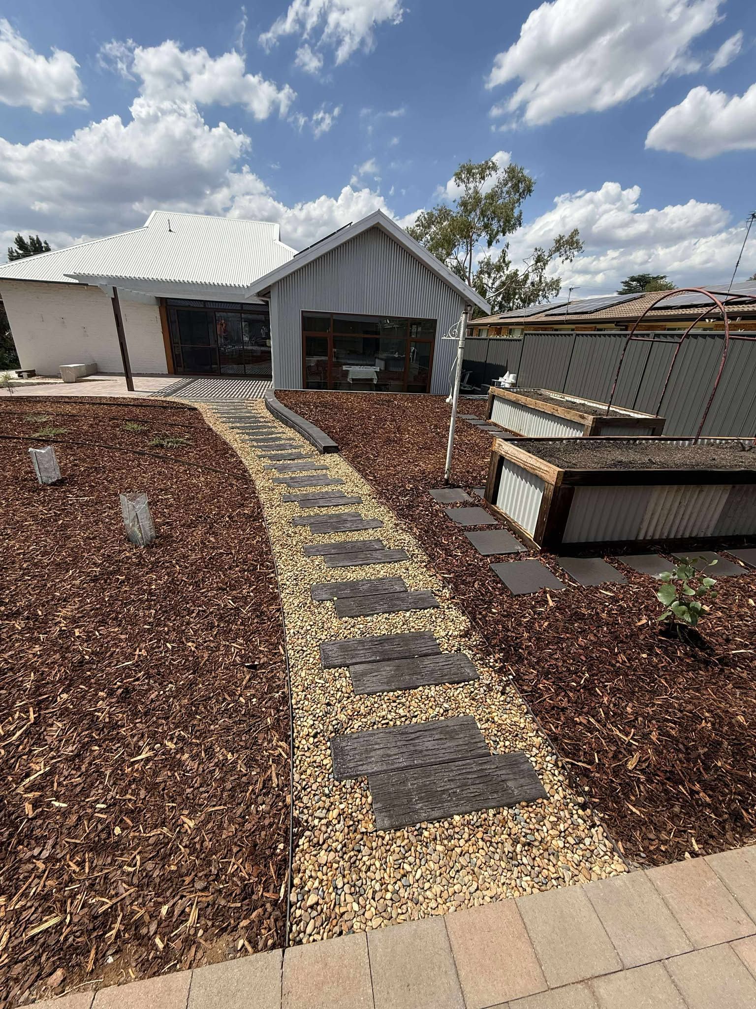 A house with a stone walkway leading to a garage with wood chips in the yard — Darlington Landscaping in Parkes, NSW