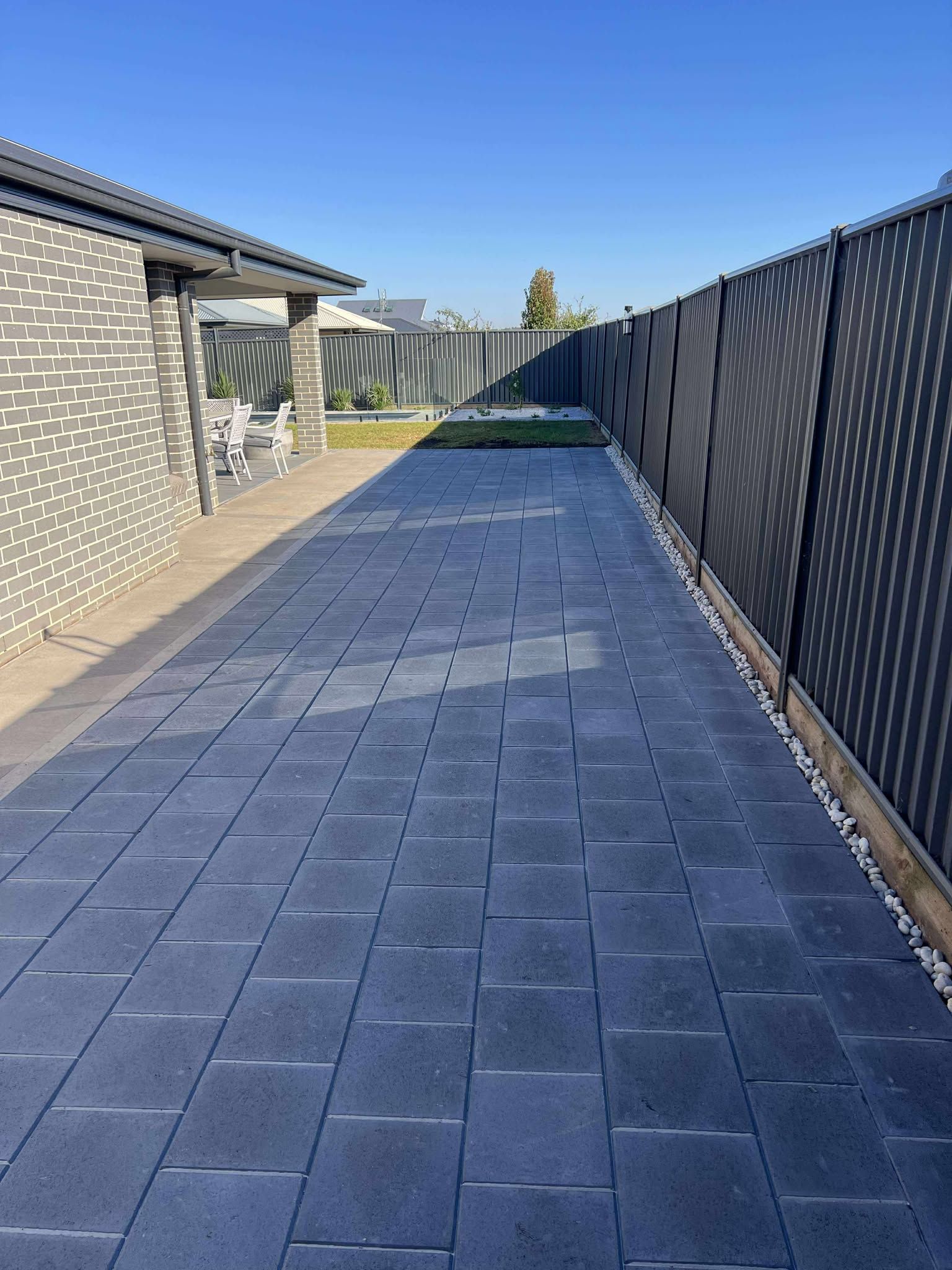A paved driveway lined with a black fence and a brick house, under a blue sky — Darlington Landscaping in Dubbo, NSW