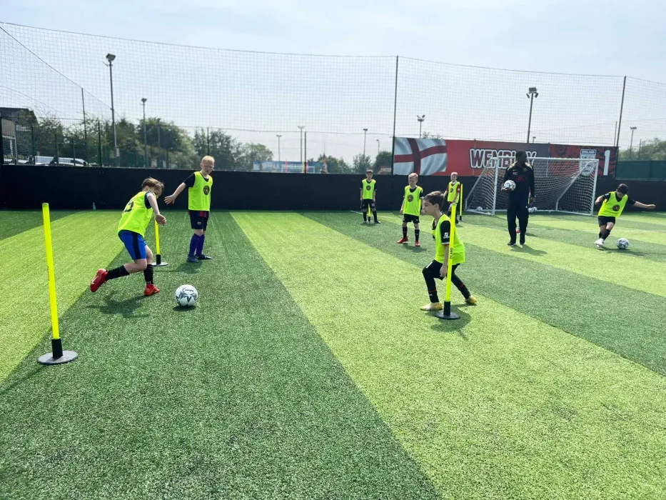 Children practicing soccer drills on an outdoor turf field with cones and a goal in the background