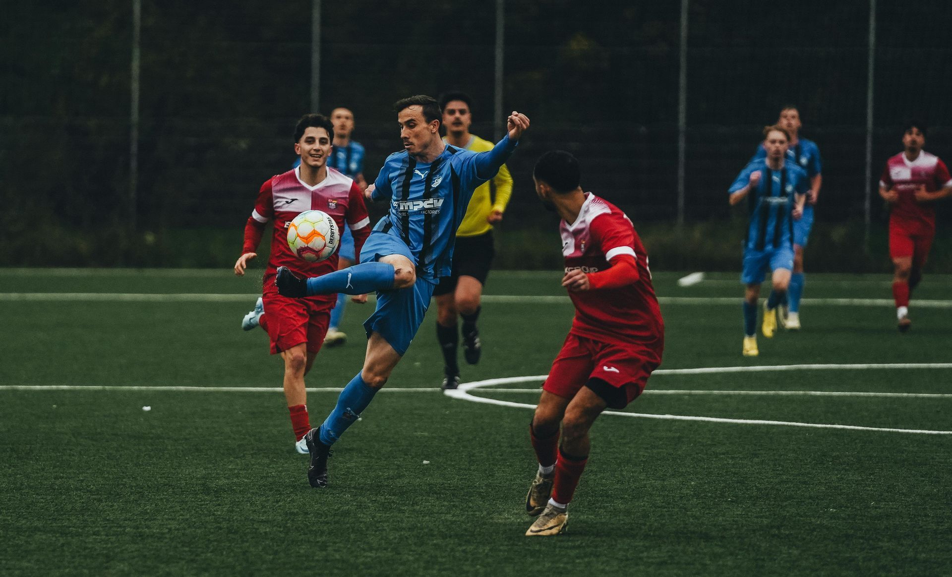 Soccer players in red and blue jerseys compete on a wet field during a match
