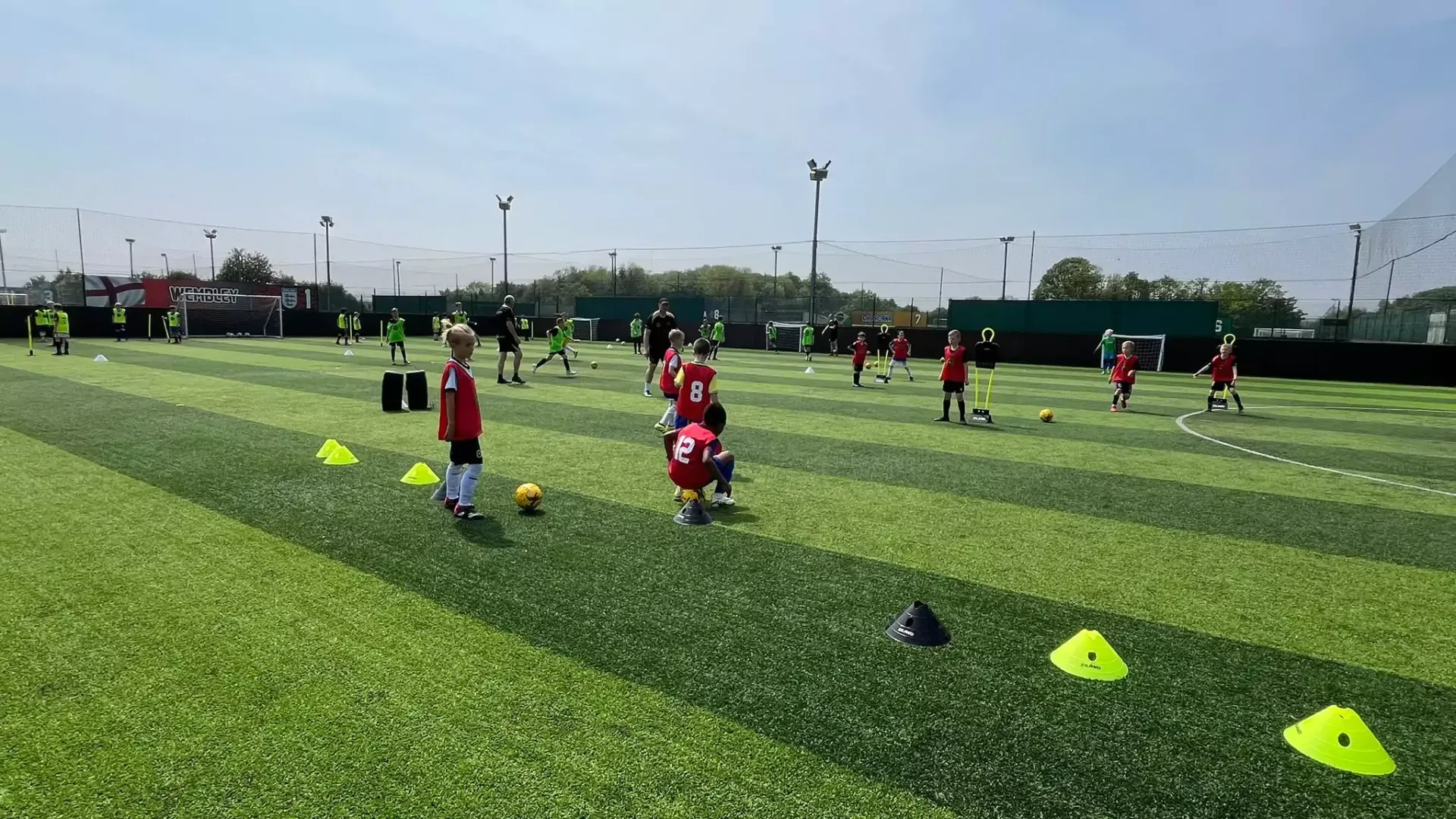 Youth soccer practice on a green field, with players in red jerseys and yellow cones under a cloudy sky