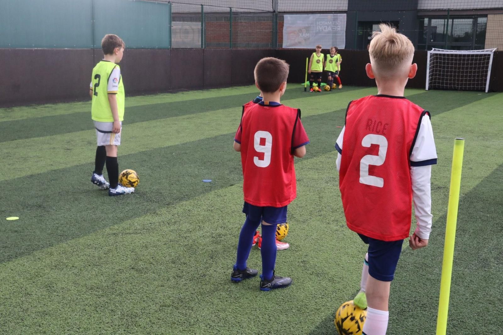 Children in red jerseys line up on a soccer field, facing a goal during practice.