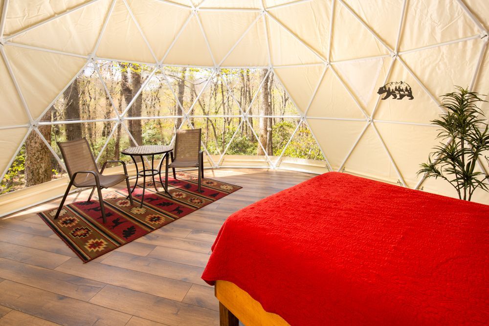 A bedroom in a dome with a bed , chairs , table and rug.