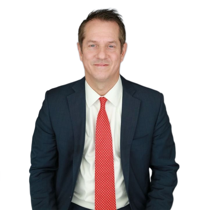 Man in a navy suit and red tie, smiling, against a gray background.