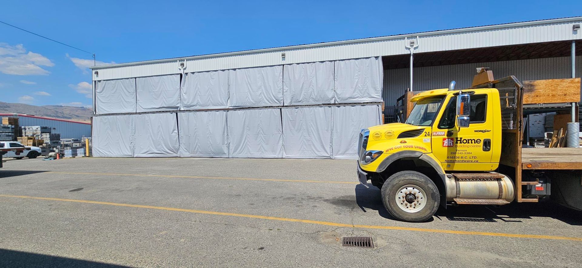 Yellow truck parked near a large white industrial building under a blue sky.