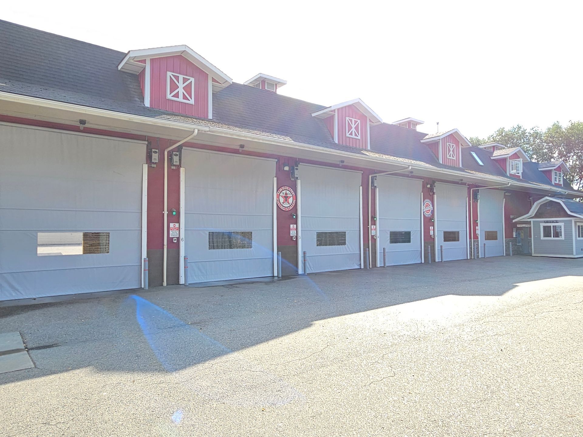 Red and white building with several gray garage doors; gravel driveway.