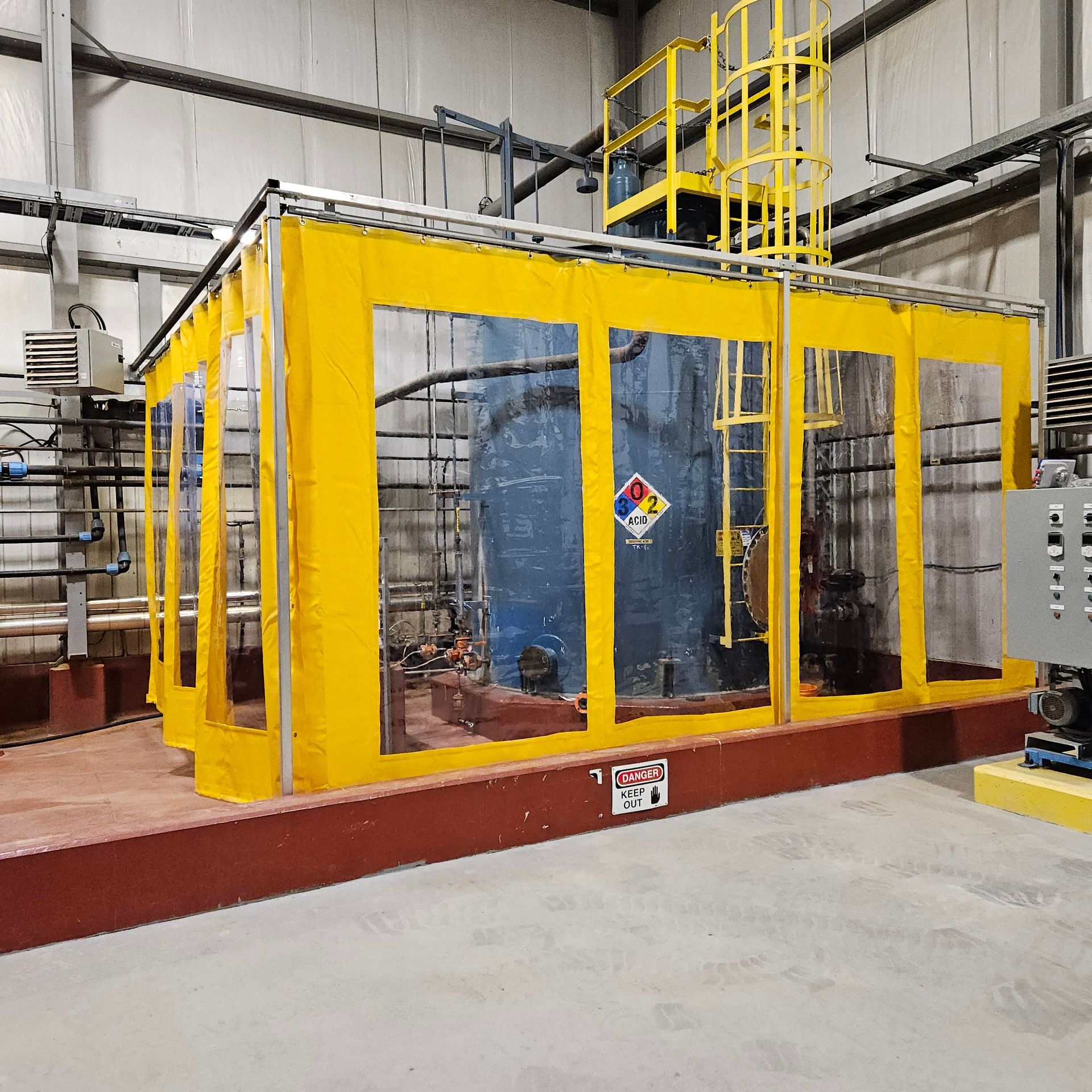 Yellow containment shelter around a blue chemical tank in a factory setting.