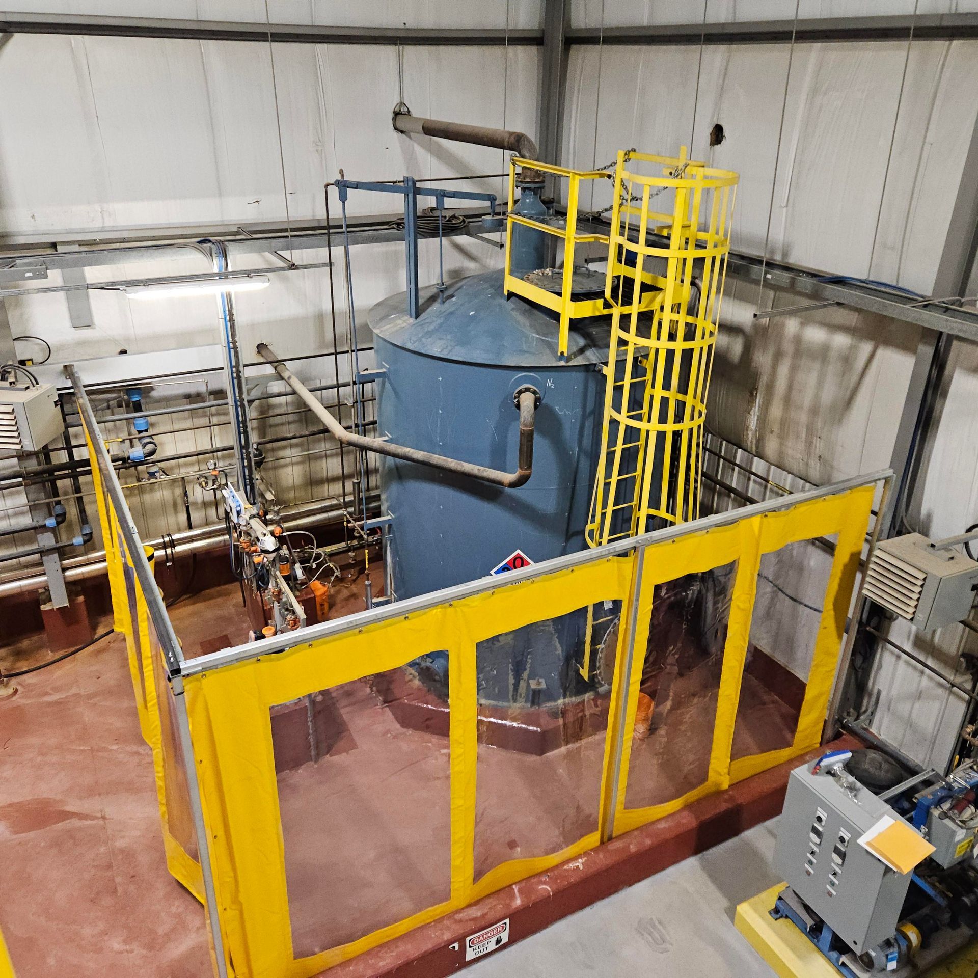 Blue industrial tank with yellow safety cage in a factory setting.