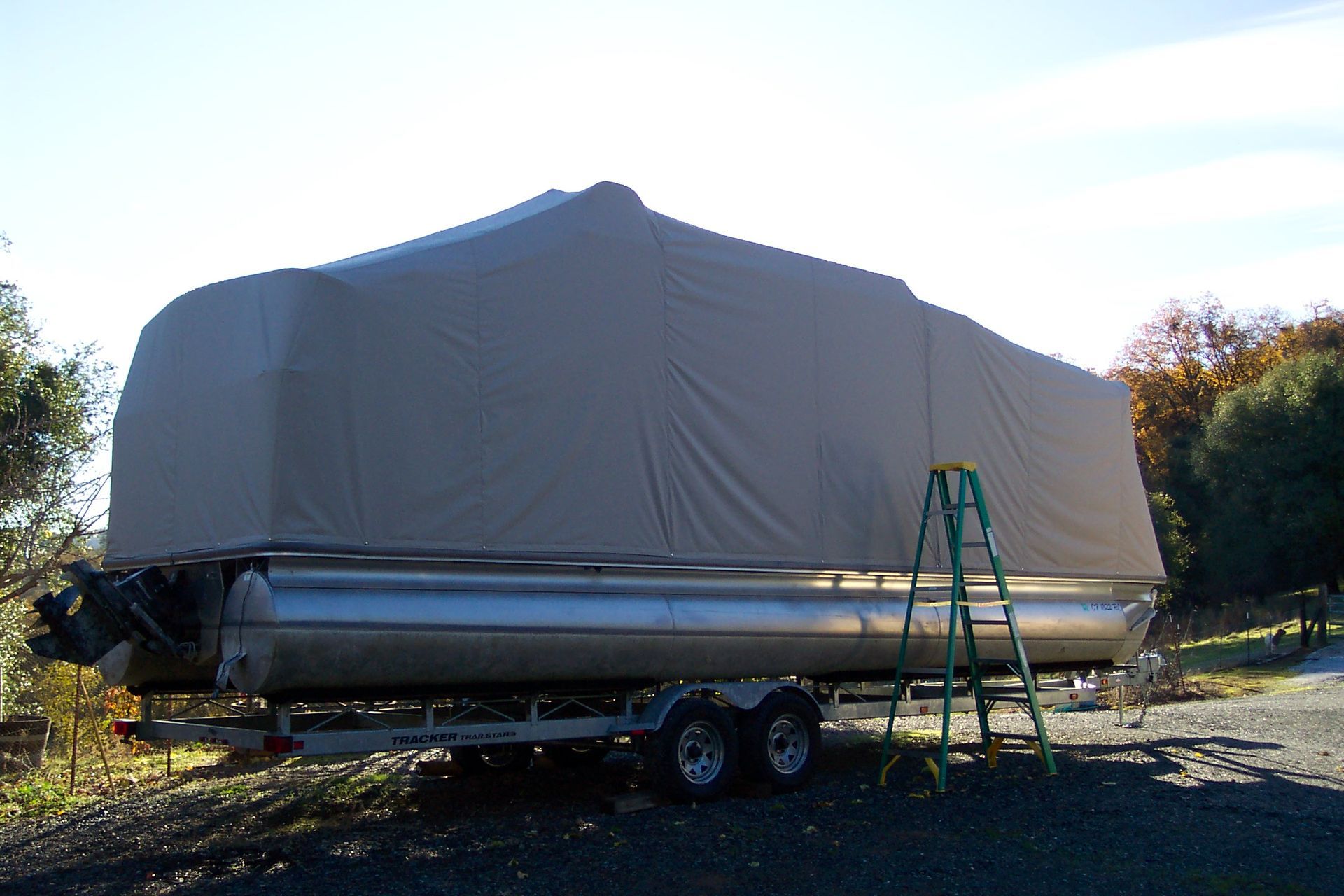 Pontoon boat covered in tan tarp on trailer, ladder alongside.