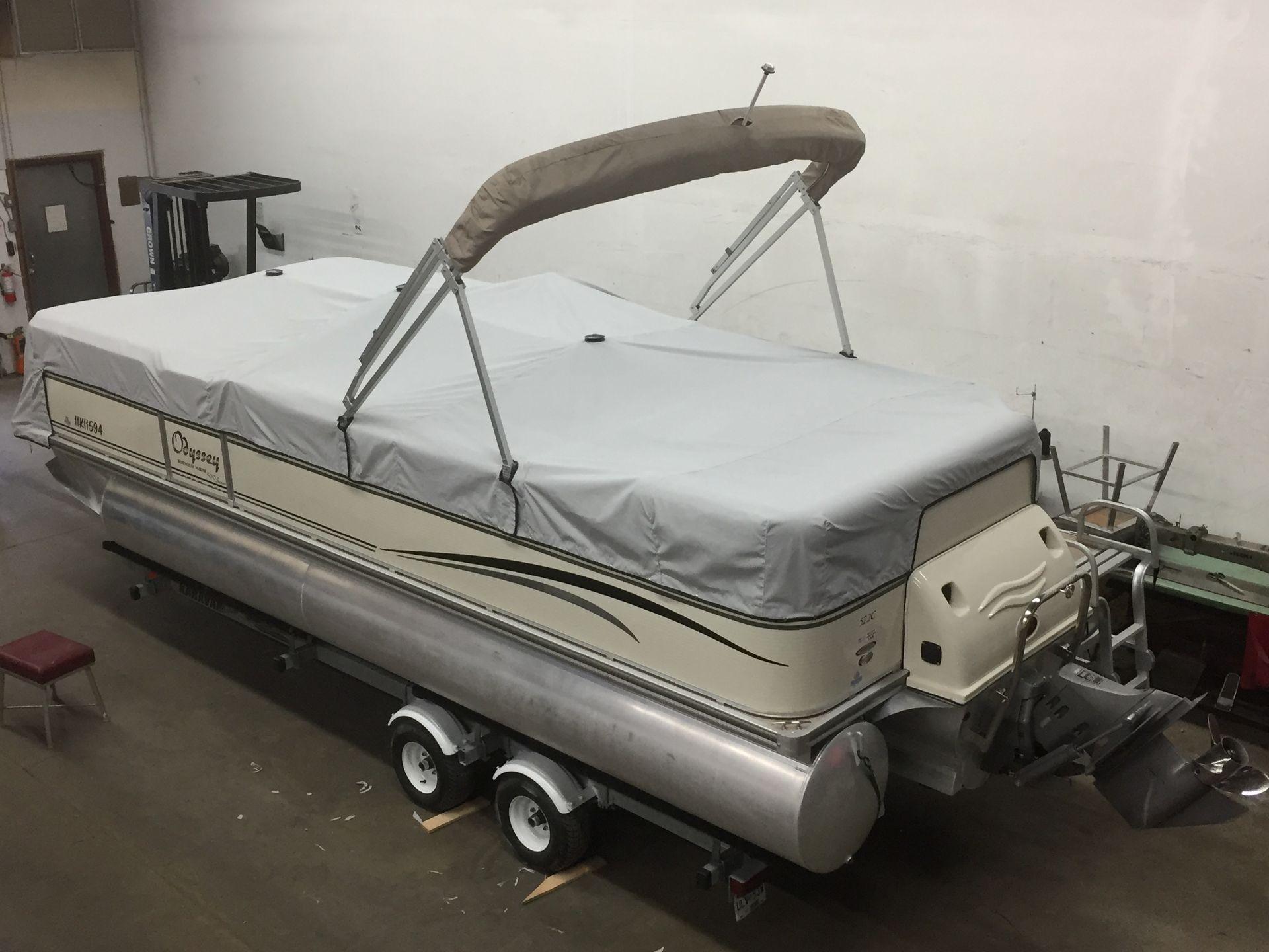 Pontoon boat with a gray cover, beige hull, and tan canopy on a trailer.