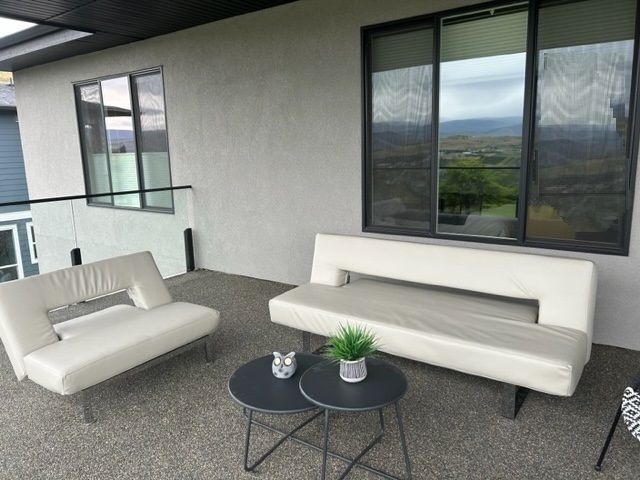 Outdoor seating area with cream-colored sofas and small black tables on a textured grey floor, overlooking a scenic view.