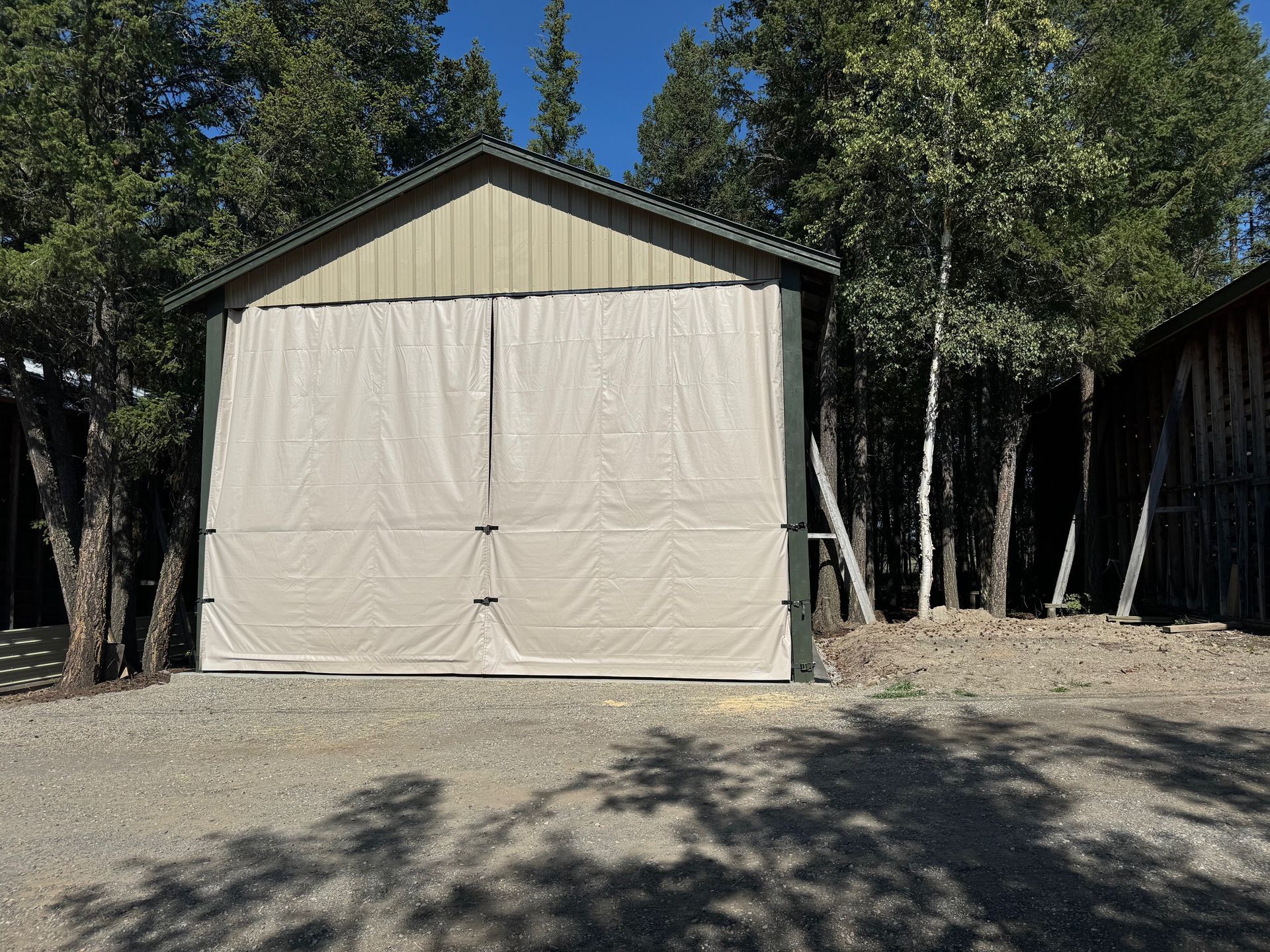 Tan curtains hang on a green shed with a corrugated roof, in front of trees.