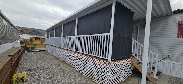 A mobile home with a screened-in porch and white lattice skirting. The sky is overcast.