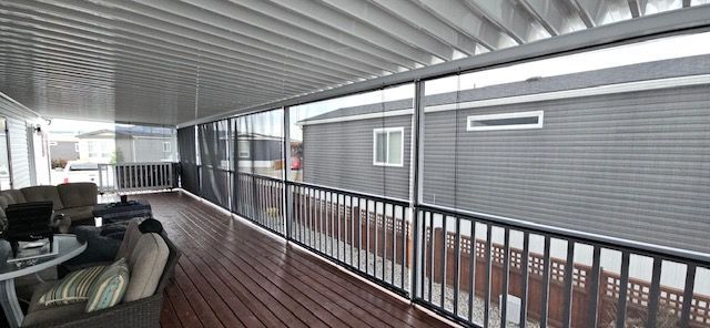 Enclosed deck with wooden floor, black railing, and gray siding visible through the screens. Furnished with a sofa and table.
