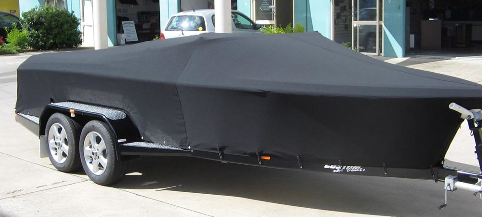 A black trailer covered with a black tarp in front of a white building.