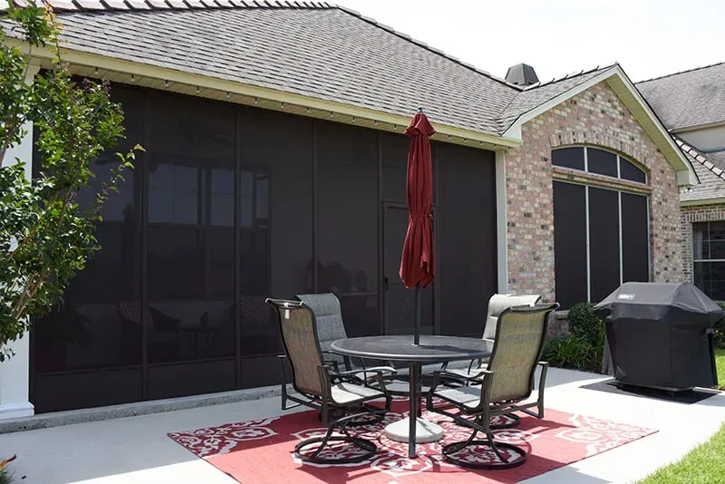 Screened patio with outdoor furniture, red umbrella, and a grill, attached to a brick house.
