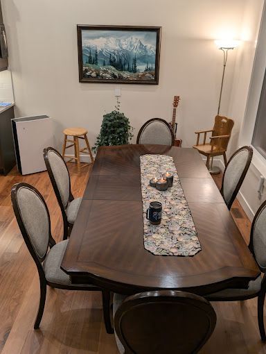 Dining room with large wooden table, chairs, artwork, and a floor lamp.