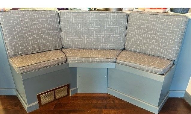 Built-in corner bench with light blue paint, three seat cushions with a gray patterned fabric.
