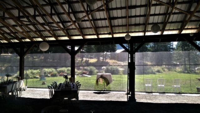 Inside of a barn looking out at a backyard, with tables and chairs set up.