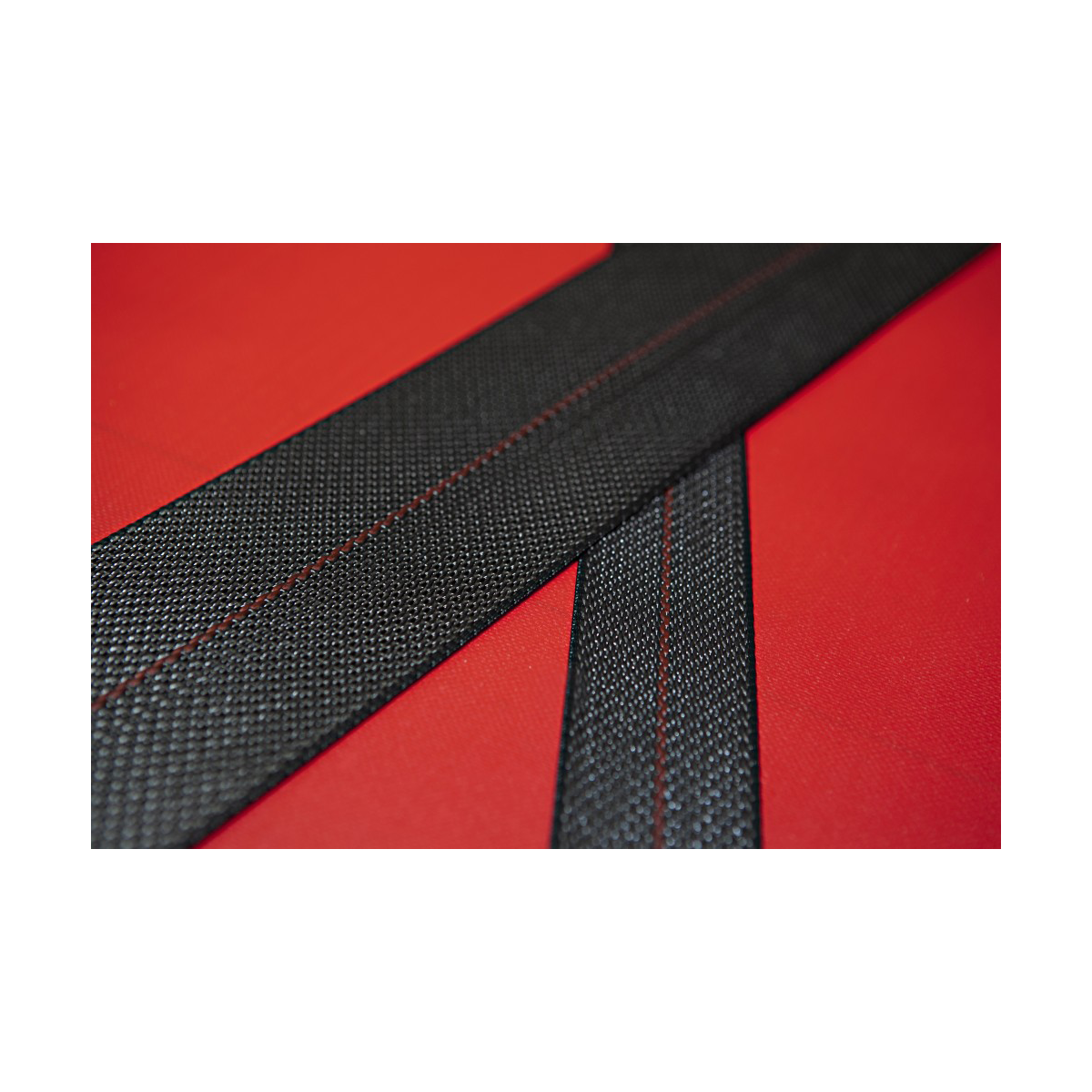 Black fabric straps with red stitching on a red surface.