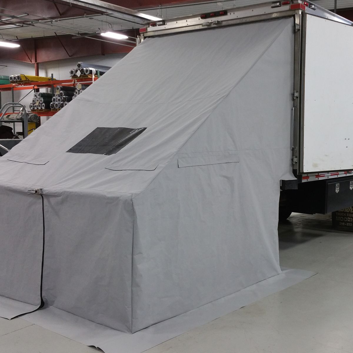 Gray fabric enclosure attached to a white truck; includes window and ground-level entry.